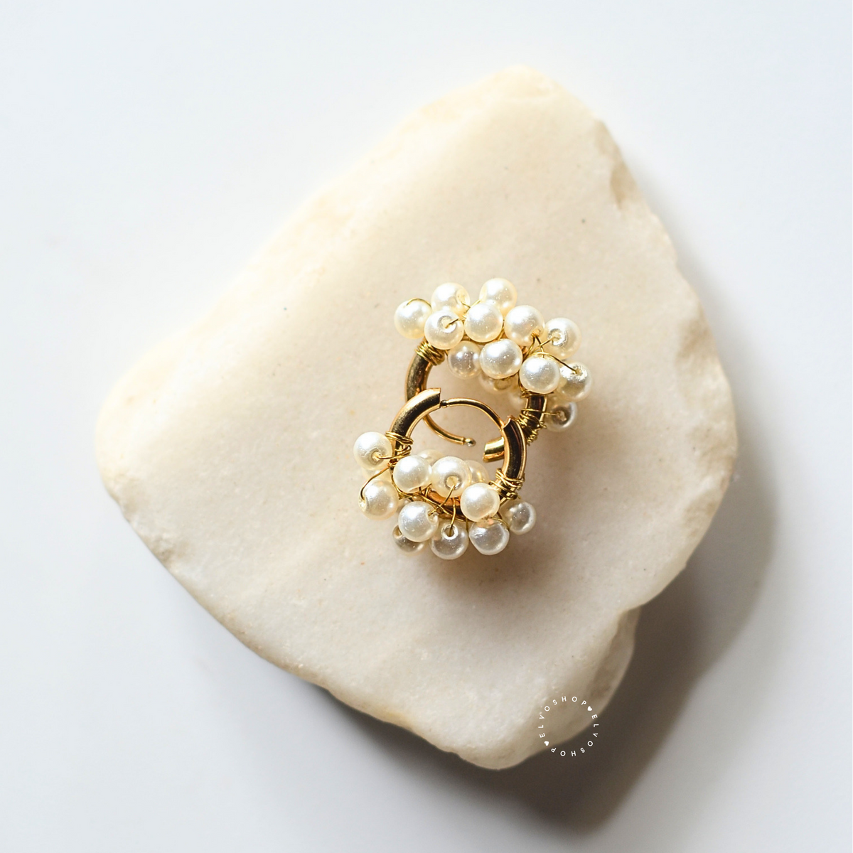 A gold ring with clusters of small white faux pearls, displayed on a light beige stone against a white background.